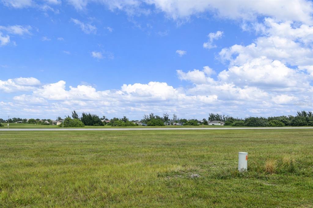 A wide, grassy vacant lot under a bright blue sky with scattered clouds — 3027 NORTHWEST 7TH TERRACE, CAPE CORAL, FL
