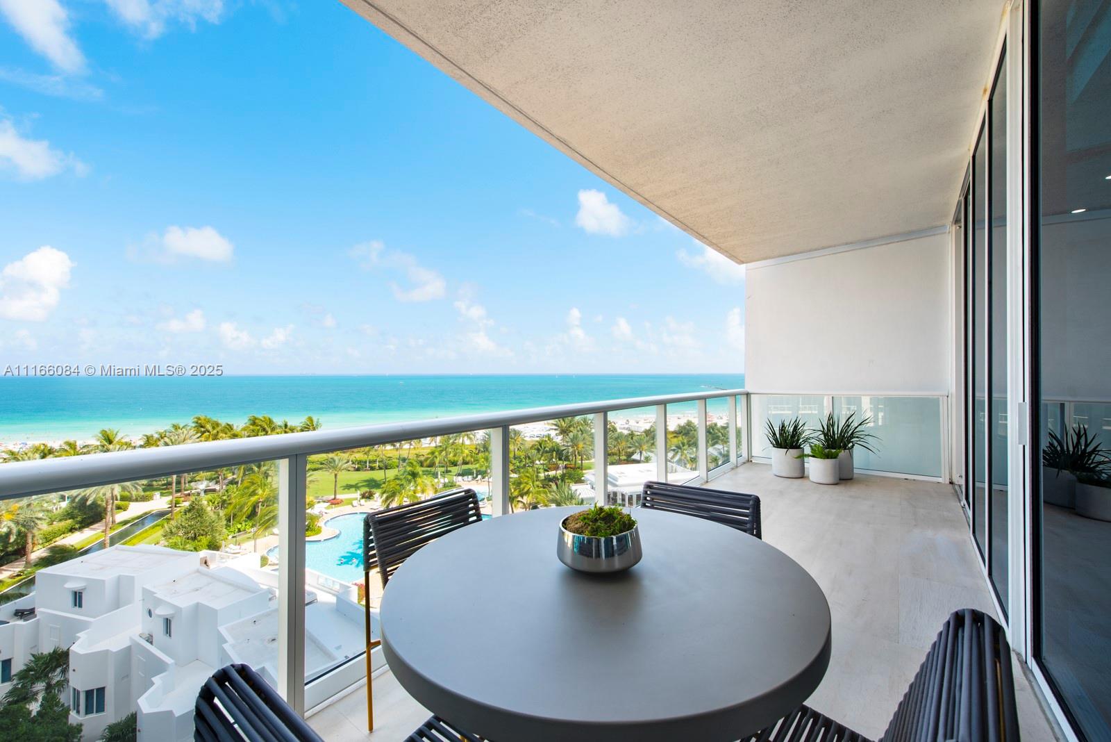 A balcony with a round table and chairs overlooks a swimming pool and the ocean — 100 S Pointe Dr # 908, Miami Beach FL 33139, MIAMI BEACH, FL