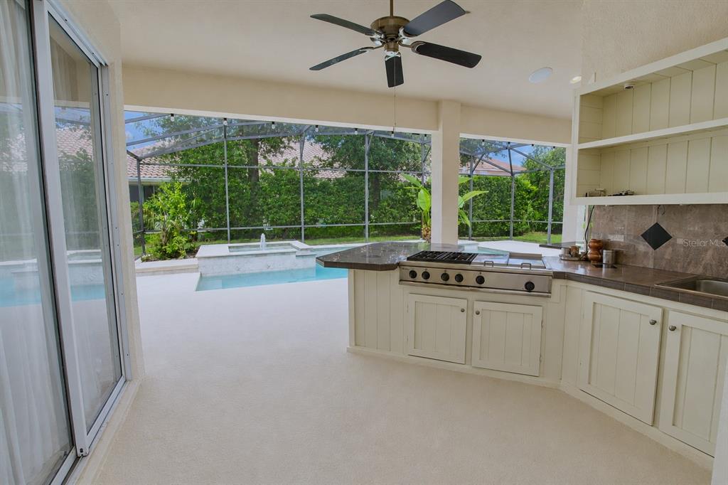 An outdoor kitchen with a grill and cabinets overlooks a screened-in pool and patio area — 1954 ELKHORN COURT, LONGWOOD, FL