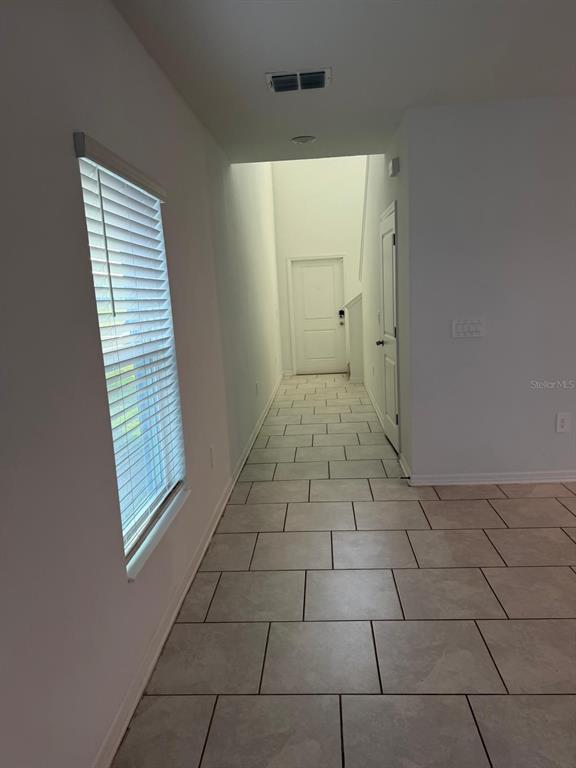A hallway with light-colored tile flooring leads to a white front door and stairs — 693 REGGIE ROAD, WINTER HAVEN, FL