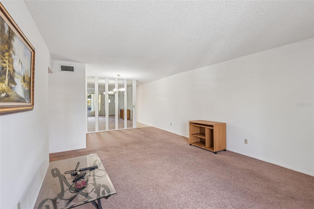 A living room with brown carpet, white walls, a glass coffee table, and mirrored dividers — 2460 PERSIAN DRIVE UNIT 44, CLEARWATER, FL