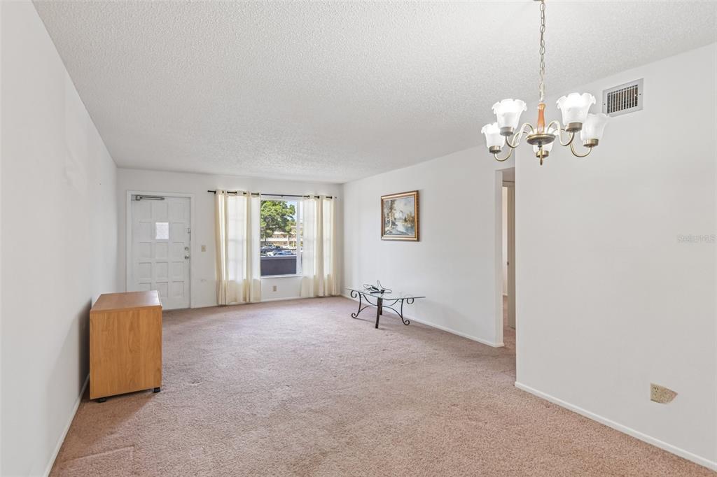 A living room with beige carpet, white walls, a chandelier, and a front door — 2460 PERSIAN DRIVE UNIT 44, CLEARWATER, FL