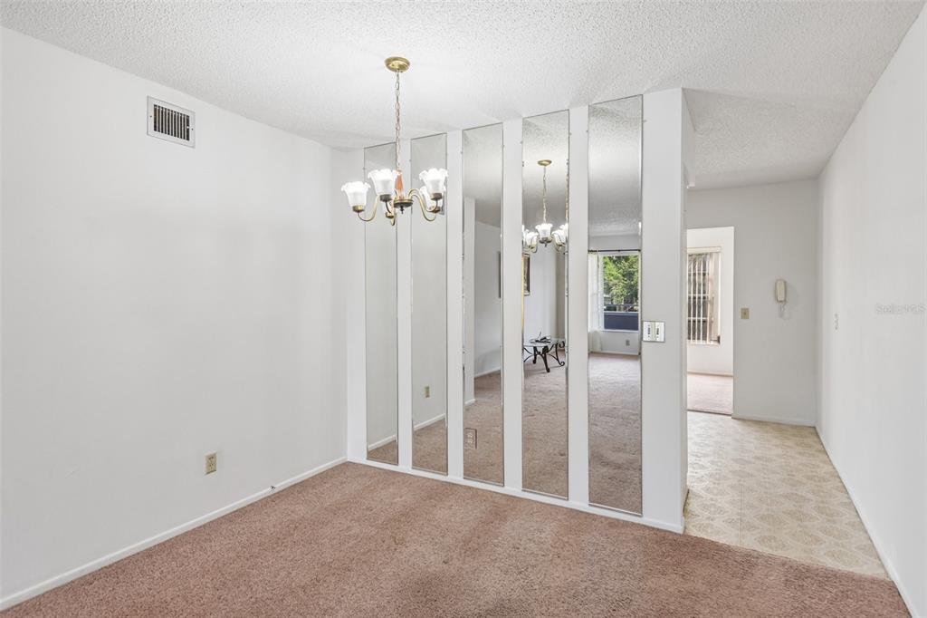 A dining area features beige carpeting, a chandelier, and a wall of vertical mirror panels — 2460 PERSIAN DRIVE UNIT 44, CLEARWATER, FL