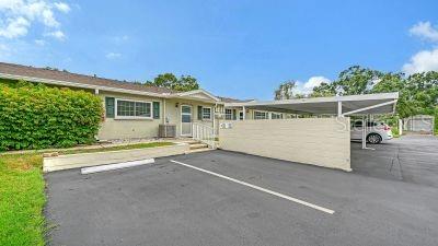 A single-story building with a carport, paved parking area, and green landscaping under a blue sky — 2436 GOLF COURSE DRIVE UNIT 707, SARASOTA, FL