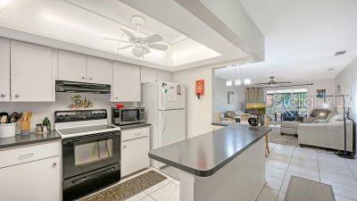 A kitchen with white cabinets and black appliances opens into a living area with tile floors — 2436 GOLF COURSE DRIVE UNIT 707, SARASOTA, FL