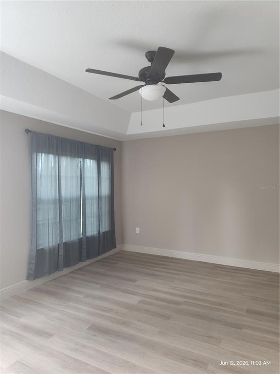 An empty bedroom features light wood-look flooring, beige walls, a tray ceiling, and a ceiling fan — 13744 SE 40TH TERRACE, SUMMERFIELD, FL