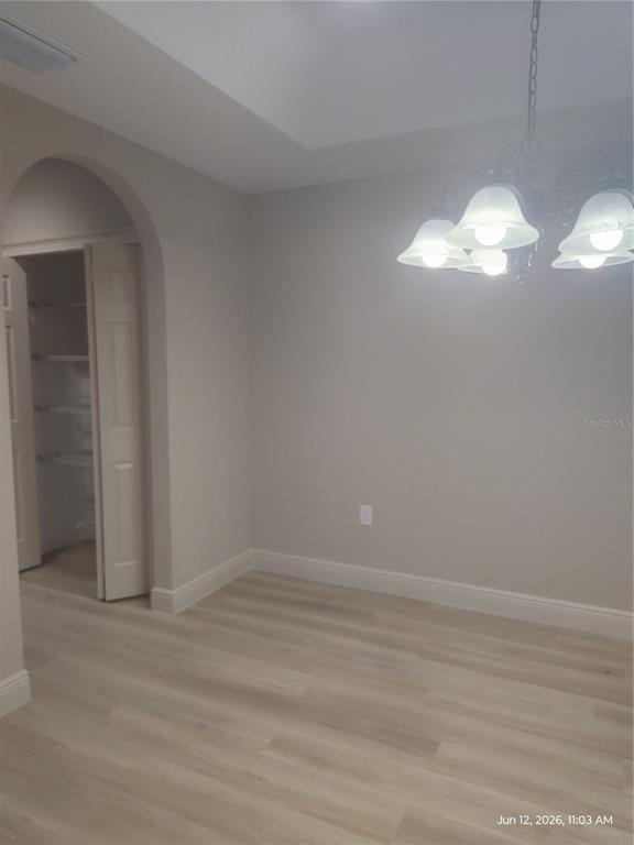 A dining room with light wood-look flooring, a chandelier, and an arched doorway to a pantry — 13744 SE 40TH TERRACE, SUMMERFIELD, FL