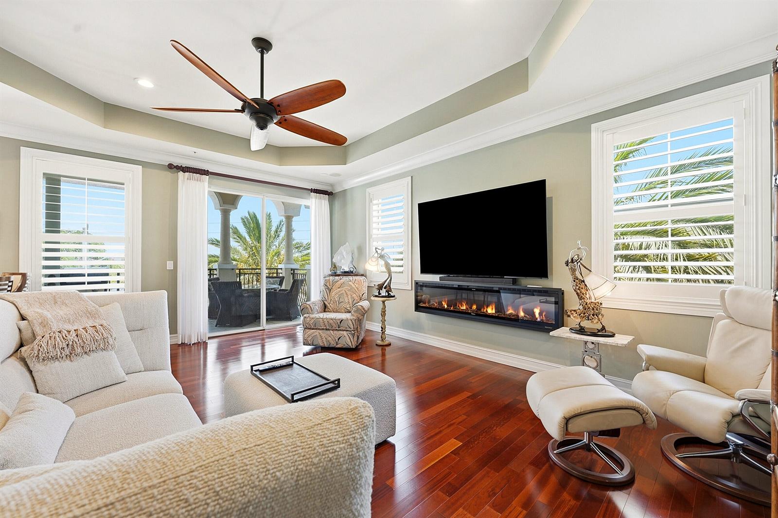 A living room with a fireplace, wall-mounted television, ceiling fan, and hardwood floors — 50 SE Ocean Boulevard # 302, Stuart FL 34994, STUART, FL
