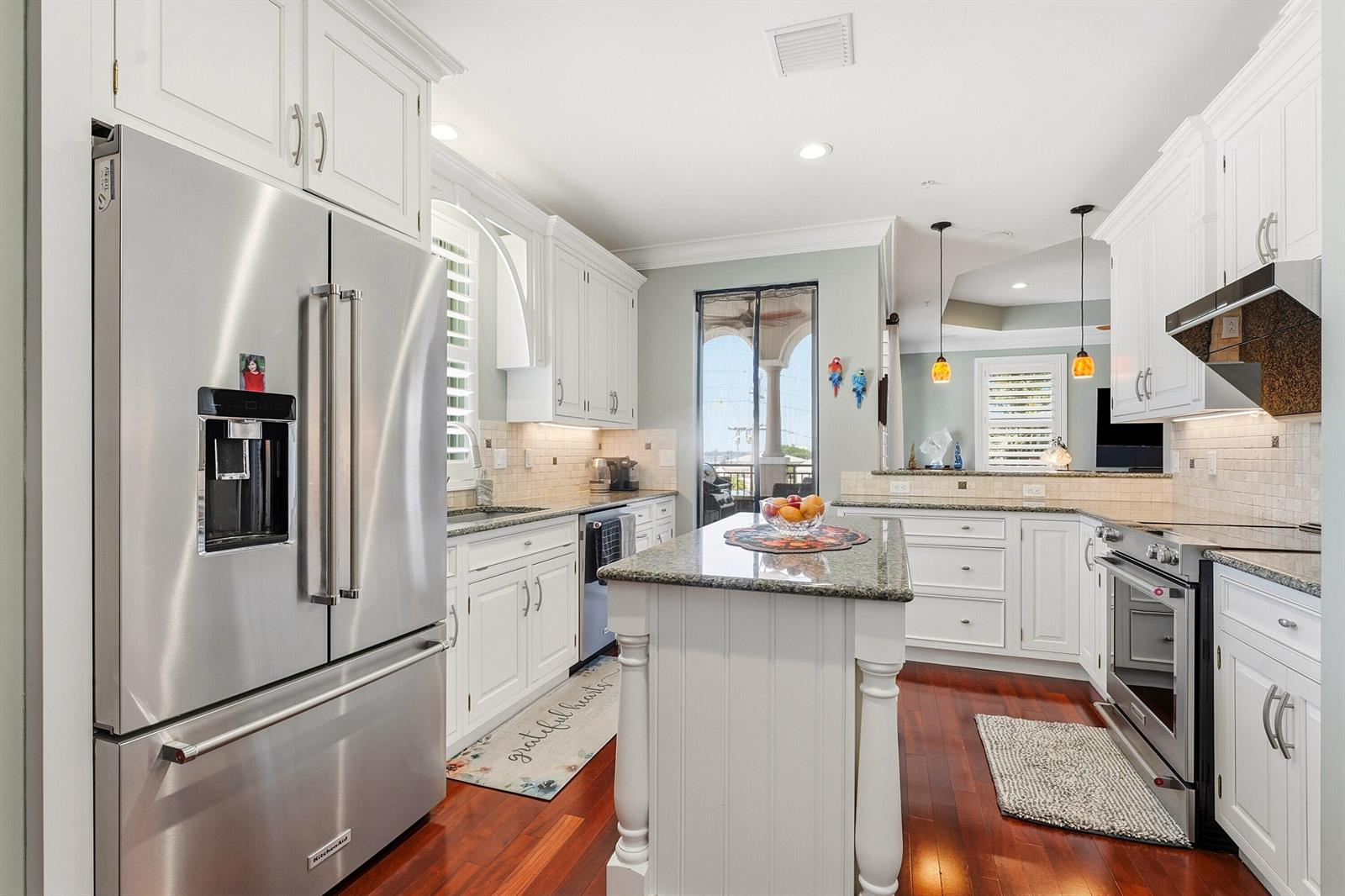 A kitchen features white cabinetry, stainless steel appliances, a granite-topped island, and hardwood floors — 50 SE Ocean Boulevard # 302, Stuart FL 34994, STUART, FL