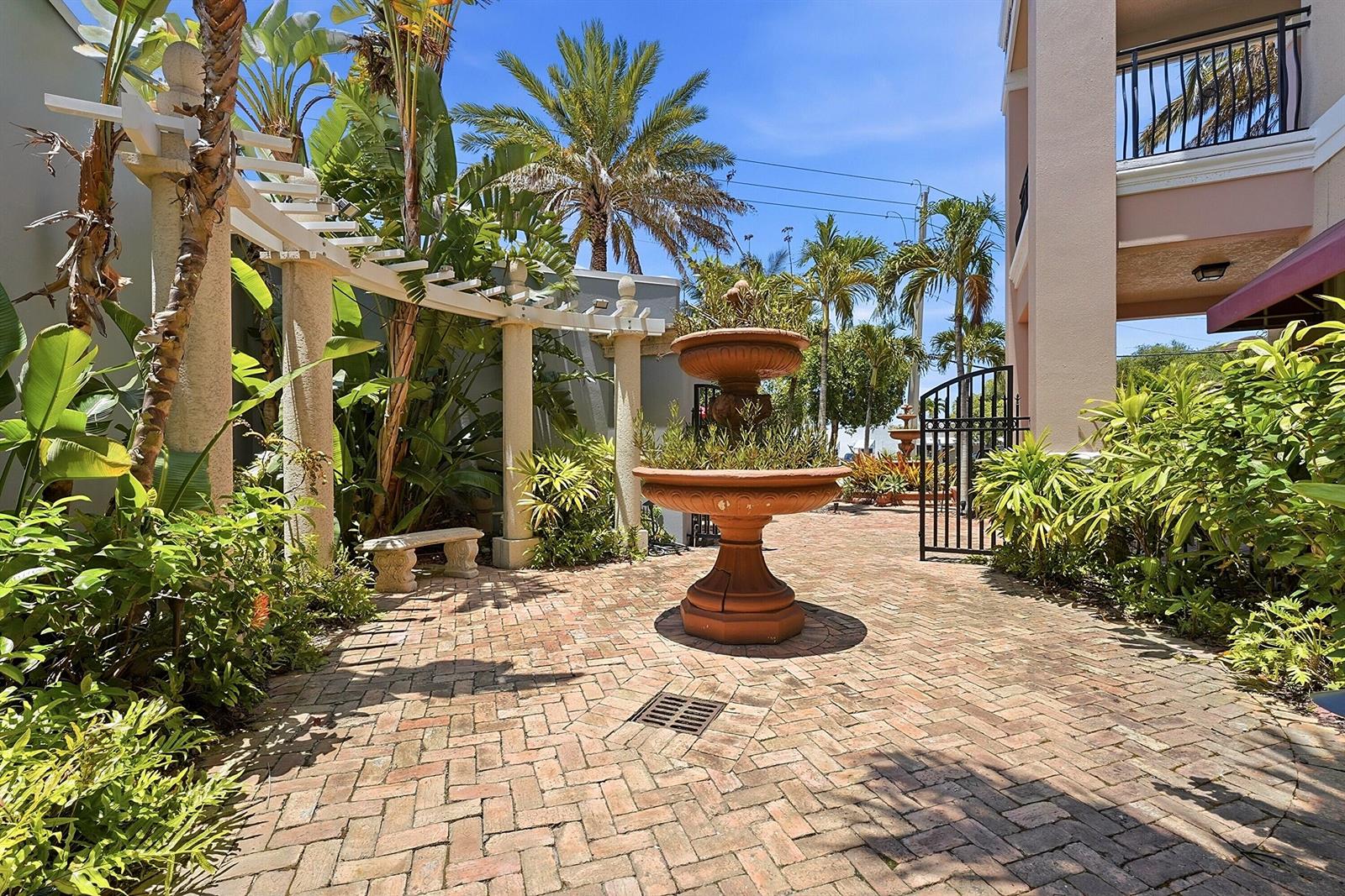 A brick courtyard features a tiered fountain, a pergola, and lush tropical landscaping — 50 SE Ocean Boulevard # 302, Stuart FL 34994, STUART, FL