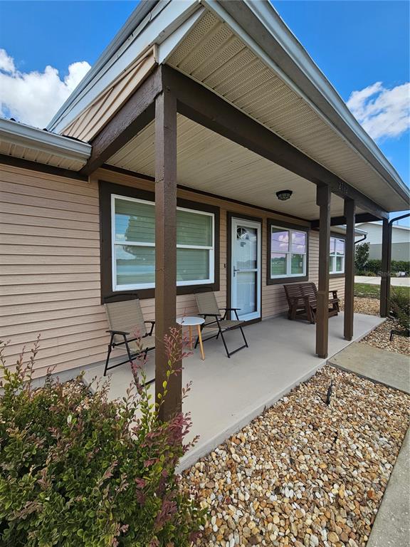 A covered front porch features tan siding, brown support posts, and a gravel yard — 2792 NAUTILUS DRIVE, AVON PARK, FL