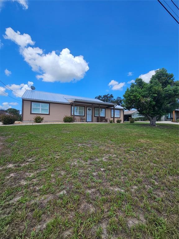 A single-story house with tan siding and a metal roof sits behind a grassy yard — 2792 NAUTILUS DRIVE, AVON PARK, FL