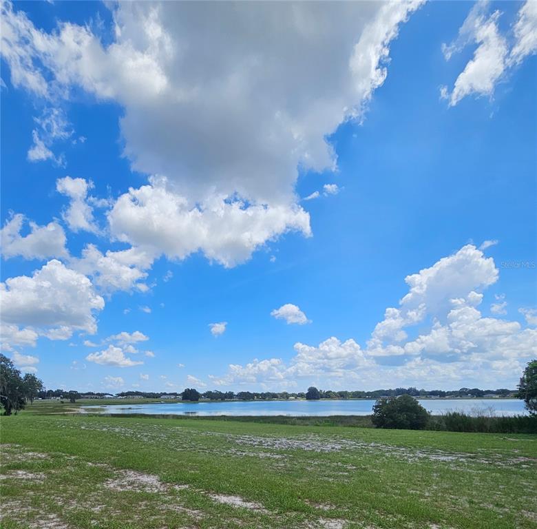 A grassy field overlooks a lake under a bright blue sky with scattered clouds — 2792 NAUTILUS DRIVE, AVON PARK, FL