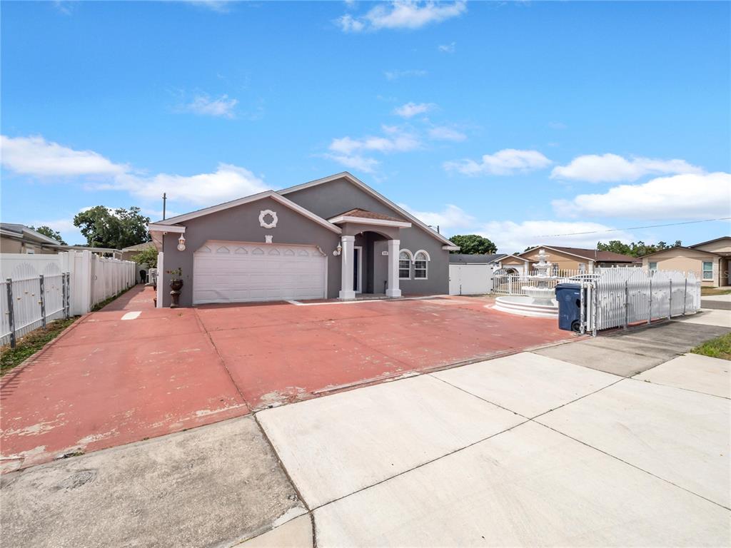 A gray single-story house features a red concrete driveway, a white garage door, and a fountain — 3122 W CREST AVENUE, TAMPA, FL