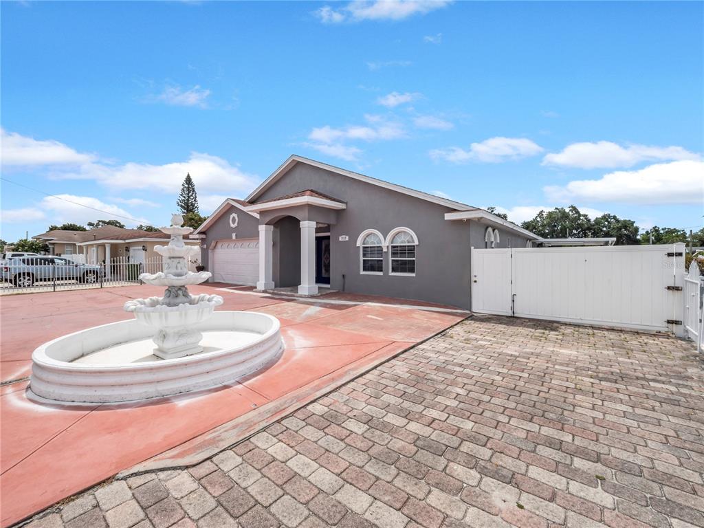 A gray house features a white tiered fountain in the front yard and paved driveway — 3122 W CREST AVENUE, TAMPA, FL