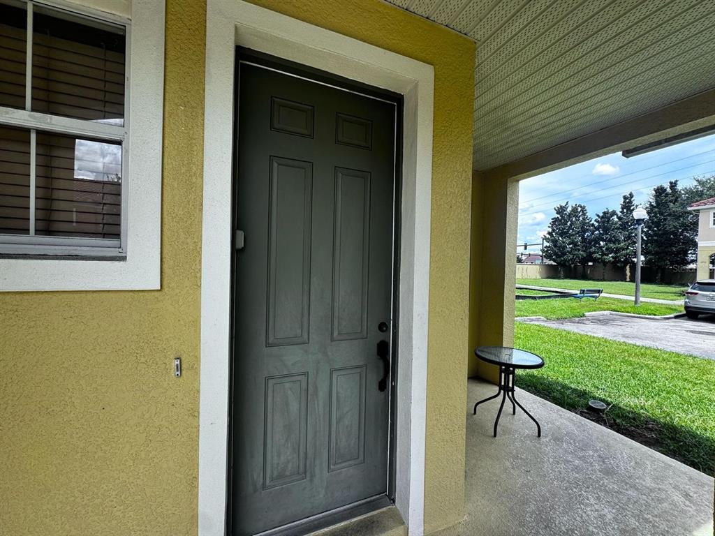 A dark gray front door sits on a yellow stucco porch next to a window — 7601 ACKLINS ROAD, KISSIMMEE, FL