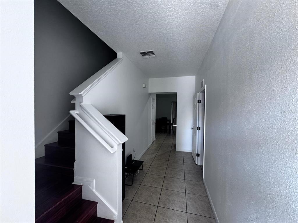 An entryway features a staircase with dark wood treads and a tiled hallway leading forward — 7601 ACKLINS ROAD, KISSIMMEE, FL