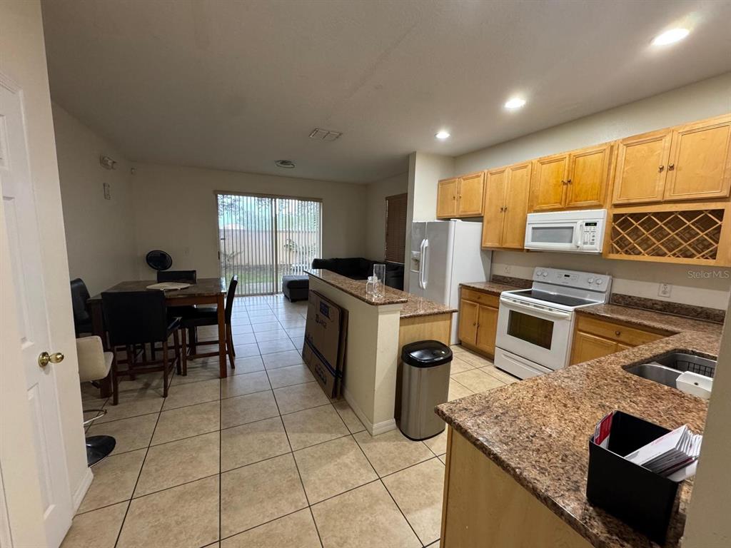 A kitchen with granite countertops and light wood cabinets opens to a dining area — 7601 ACKLINS ROAD, KISSIMMEE, FL