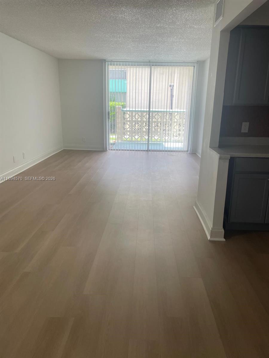 An empty living room features light wood-look flooring and a sliding glass door to a balcony — 2029 NW 46th Ave # E107, Lauderhill FL 33313, LAUDERHILL, FL