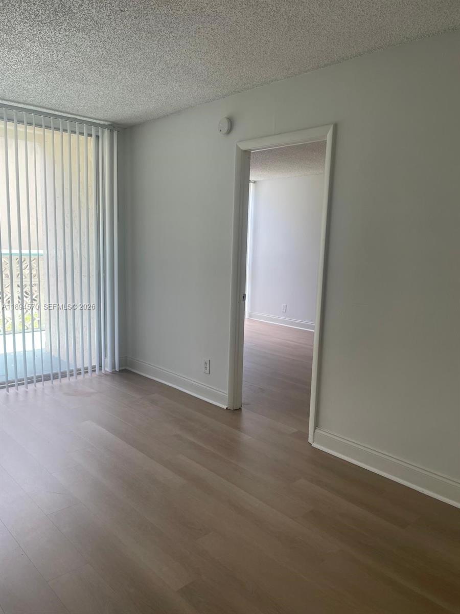 A room with light wood-look flooring and vertical blinds leads to an adjacent bedroom — 2029 NW 46th Ave # E107, Lauderhill FL 33313, LAUDERHILL, FL