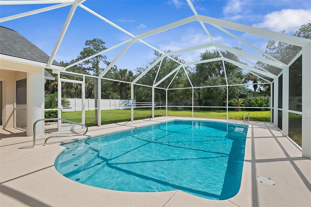 A swimming pool with a screen enclosure sits on a concrete patio in a backyard — 14 COLECHESTER LANE, PALM COAST, FL