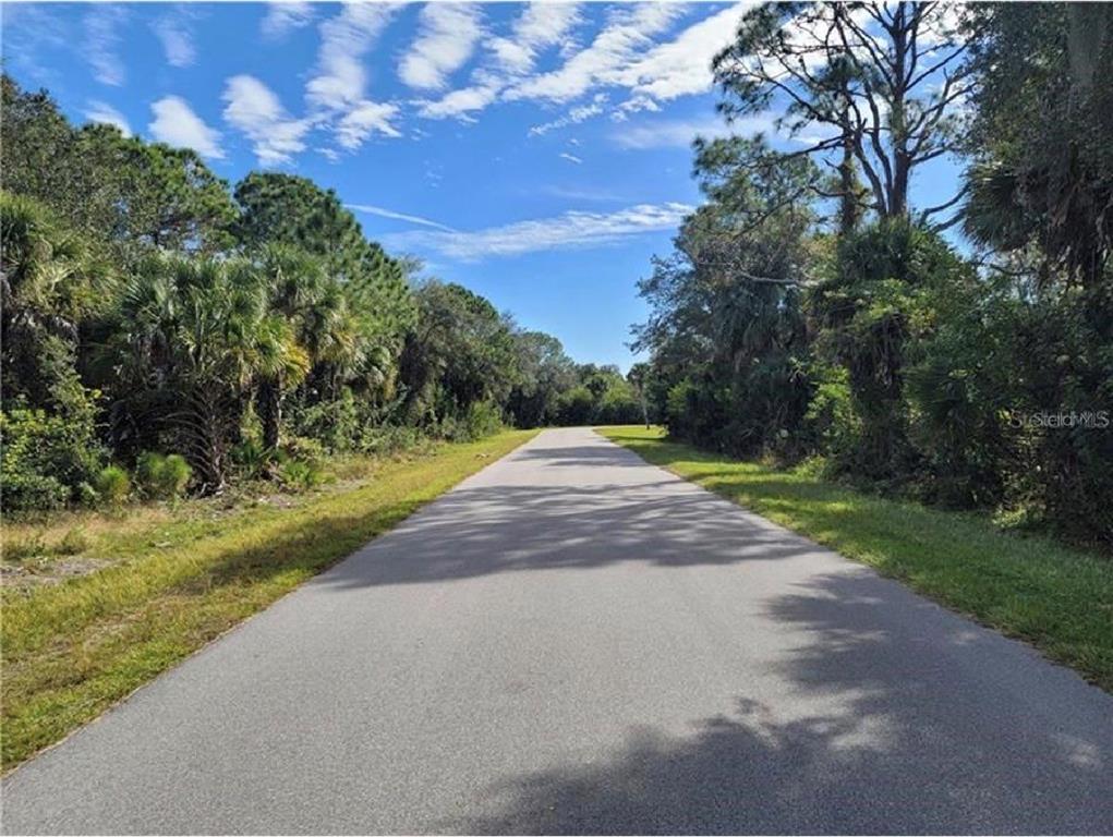 A paved road stretches forward through a wooded area under a blue sky — 520 MCDILL DRIVE, PORT CHARLOTTE, FL