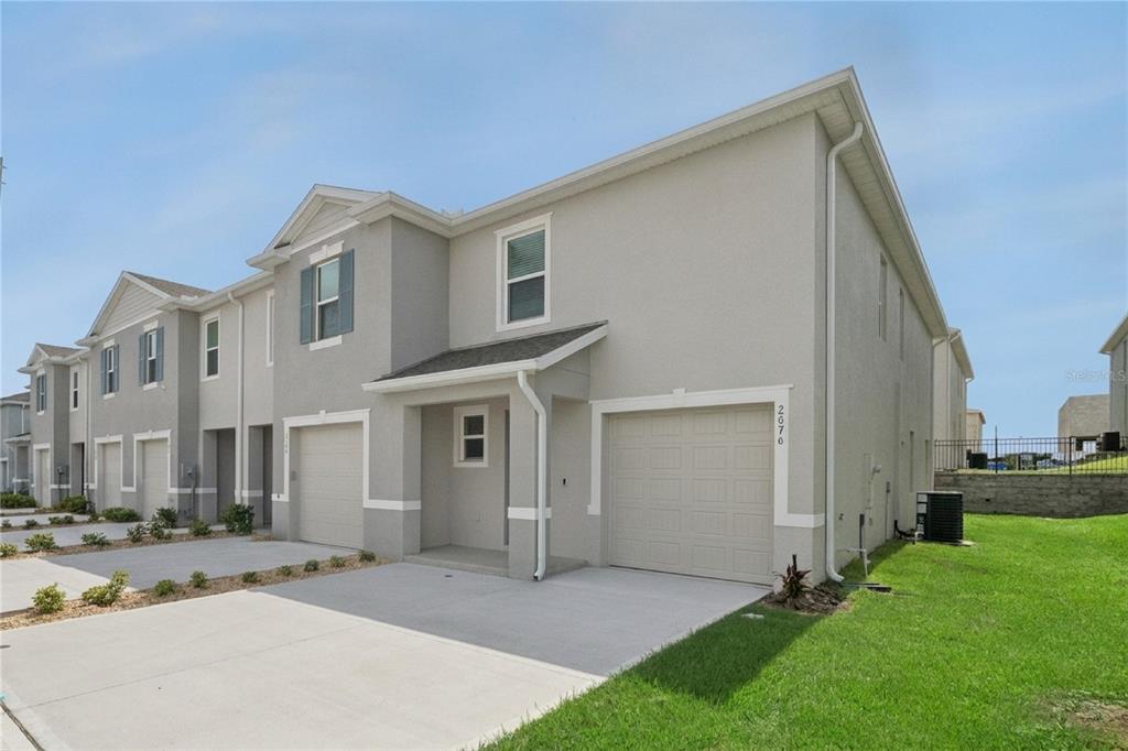 A two-story townhouse with a light gray stucco exterior, a single-car garage, and a driveway — 2076 MONTEVERDE AVENUE, DAVENPORT, FL