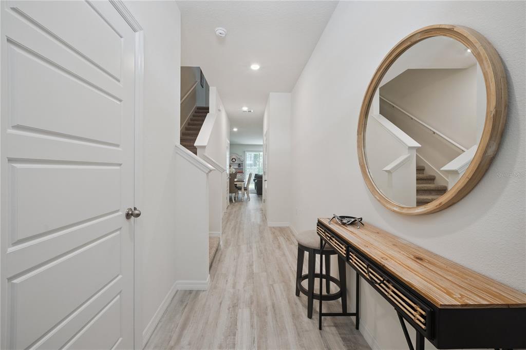 A bright entryway features light wood-look flooring, a round mirror, and a console table — 2076 MONTEVERDE AVENUE, DAVENPORT, FL
