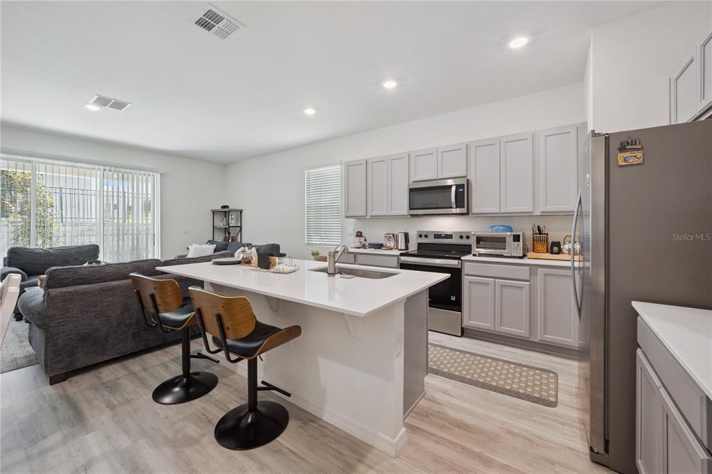 A kitchen with light gray cabinets, white countertops, and an island with two bar stools — 2076 MONTEVERDE AVENUE, DAVENPORT, FL