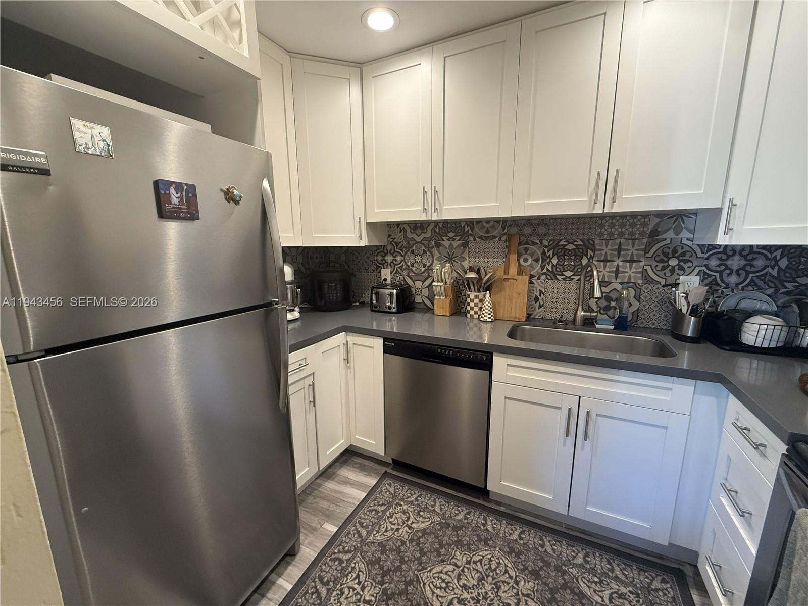 A kitchen features white cabinets, stainless steel appliances, gray countertops, and a patterned tile backsplash — 7823 Miller Dr # C207, Miami FL 33155, MIAMI, FL