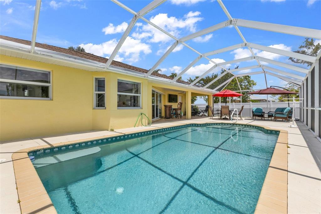 A swimming pool sits on a patio enclosed by a white screen cage behind a house — 18075 PETOSKEY CIRCLE, PORT CHARLOTTE, FL