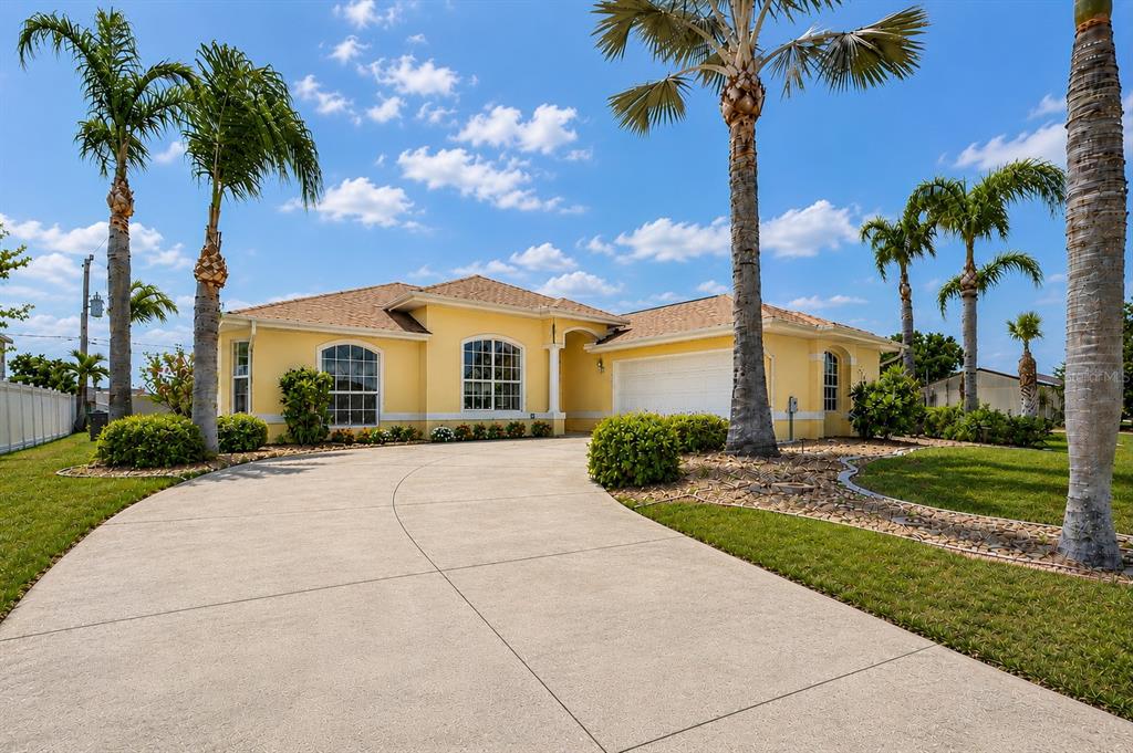 A yellow single-story house with a concrete driveway and palm trees under a blue sky — 18075 PETOSKEY CIRCLE, PORT CHARLOTTE, FL
