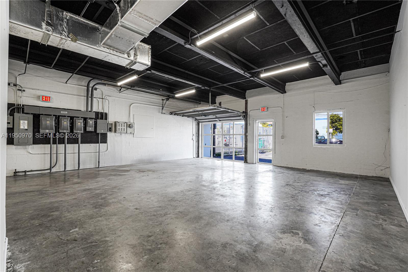 An industrial warehouse space with a concrete floor, exposed ceiling, and a roll-up door — 1822 NW 22nd St, Miami FL 33142, MIAMI, FL