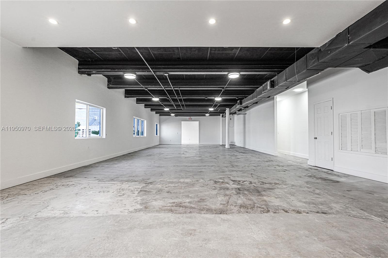 An open-plan commercial space features a concrete floor, exposed black ceiling beams, and white walls — 1822 NW 22nd St, Miami FL 33142, MIAMI, FL