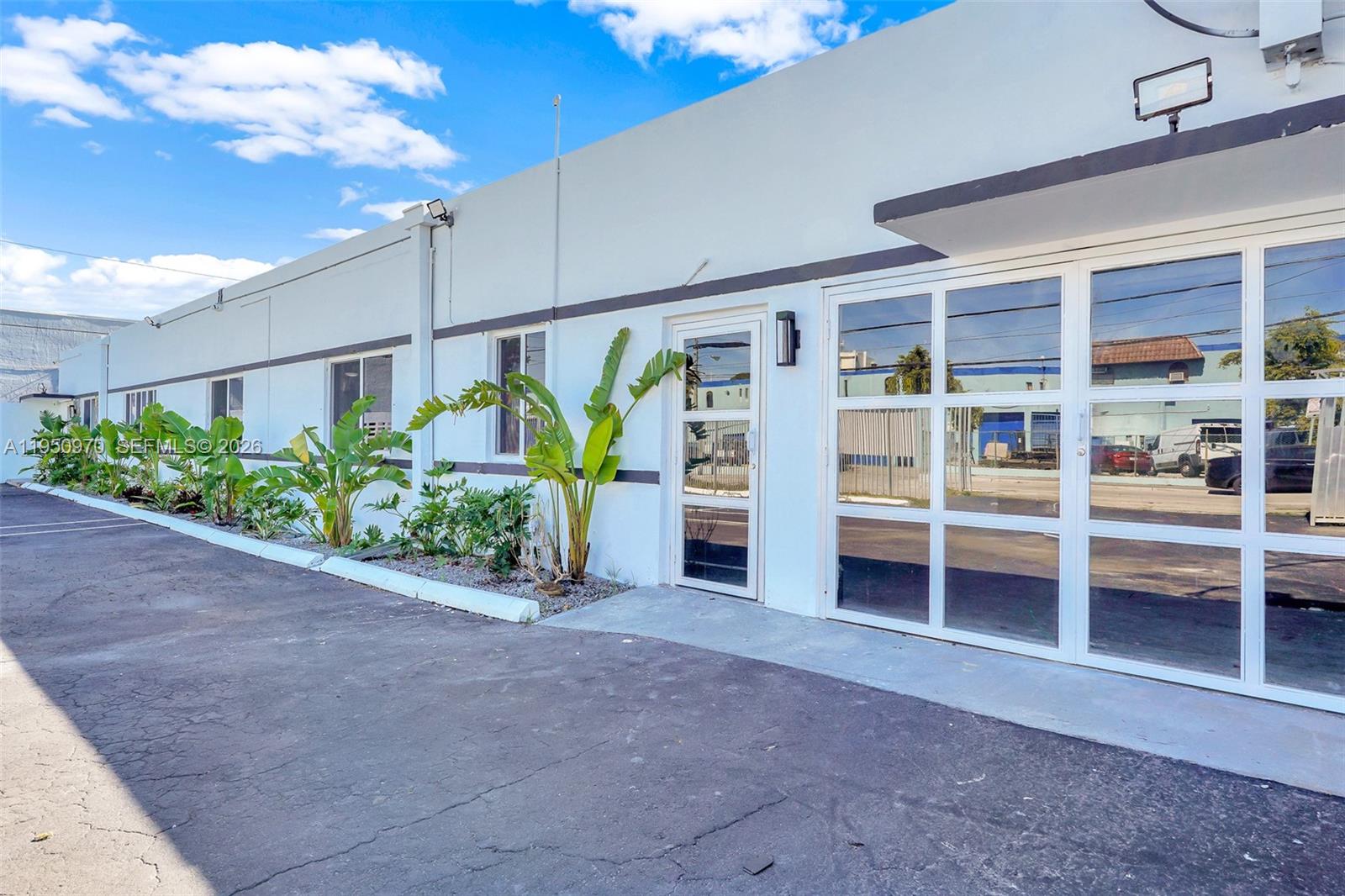 The exterior of a white commercial building features a glass door and large windows — 1822 NW 22nd St, Miami FL 33142, MIAMI, FL