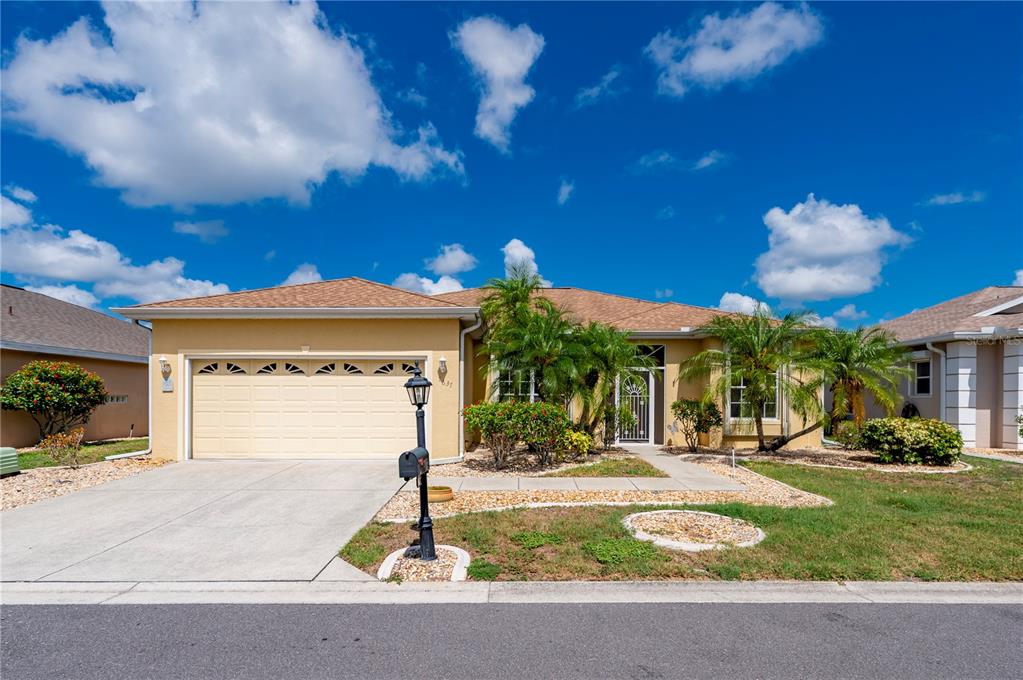 A single-story tan house with a two-car garage, palm trees, and a paved driveway — 1637 PALACE COURT, PORT CHARLOTTE, FL