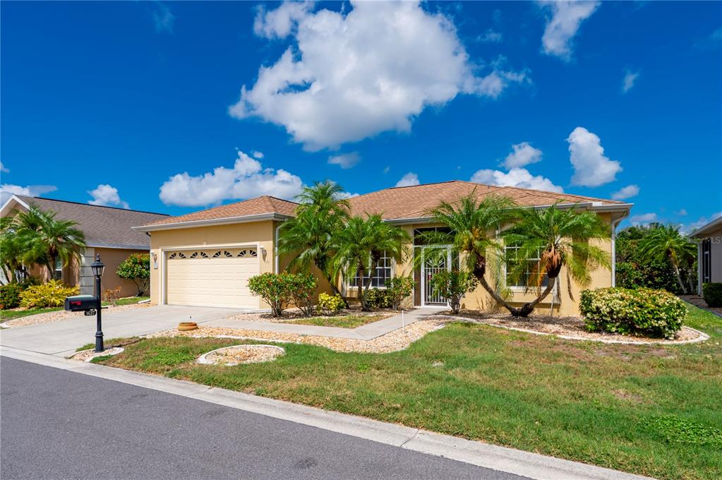 A single-story suburban house with a tan stucco exterior, a two-car garage, and palm trees — 1637 PALACE COURT, PORT CHARLOTTE, FL