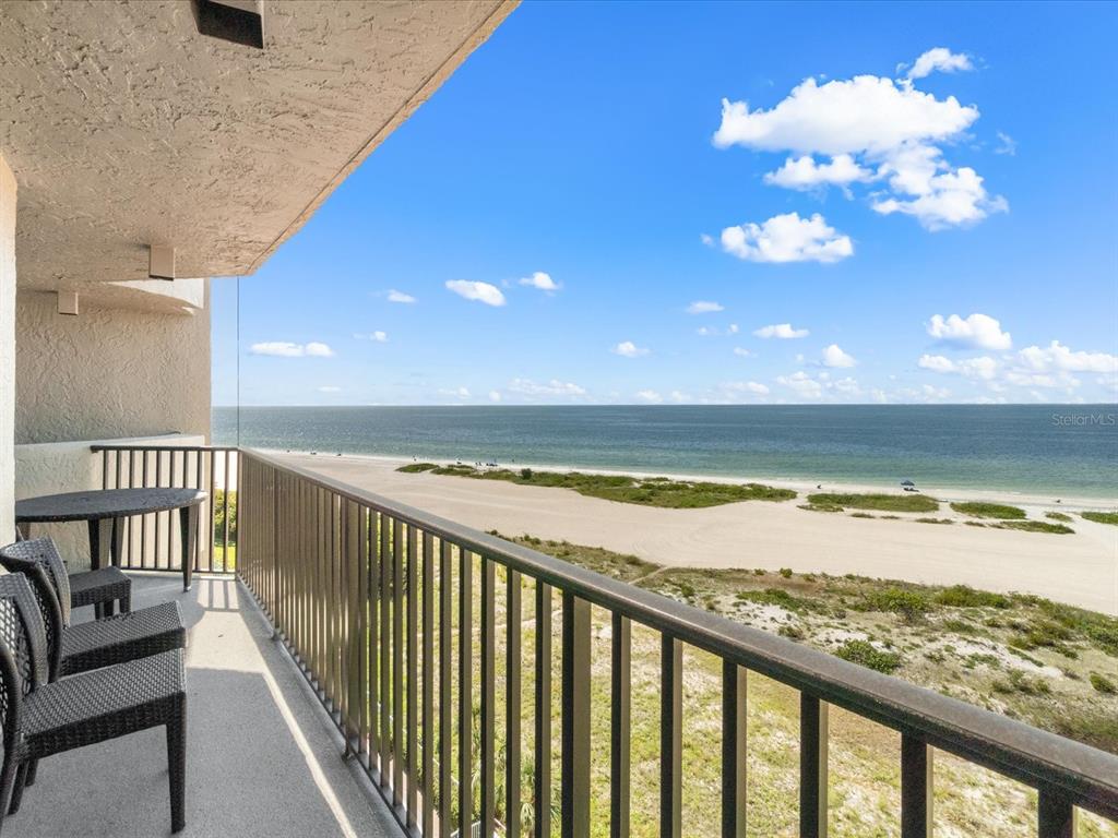A balcony with patio furniture overlooks a sandy beach and the ocean under a blue sky — 1290 GULF BOULEVARD UNIT 903, CLEARWATER BEACH, FL