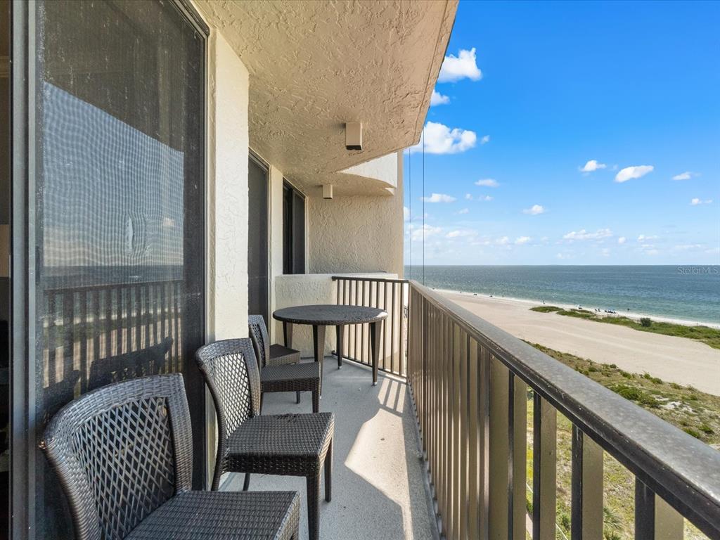A balcony with outdoor furniture overlooks a sandy beach and the ocean under blue skies — 1290 GULF BOULEVARD UNIT 903, CLEARWATER BEACH, FL