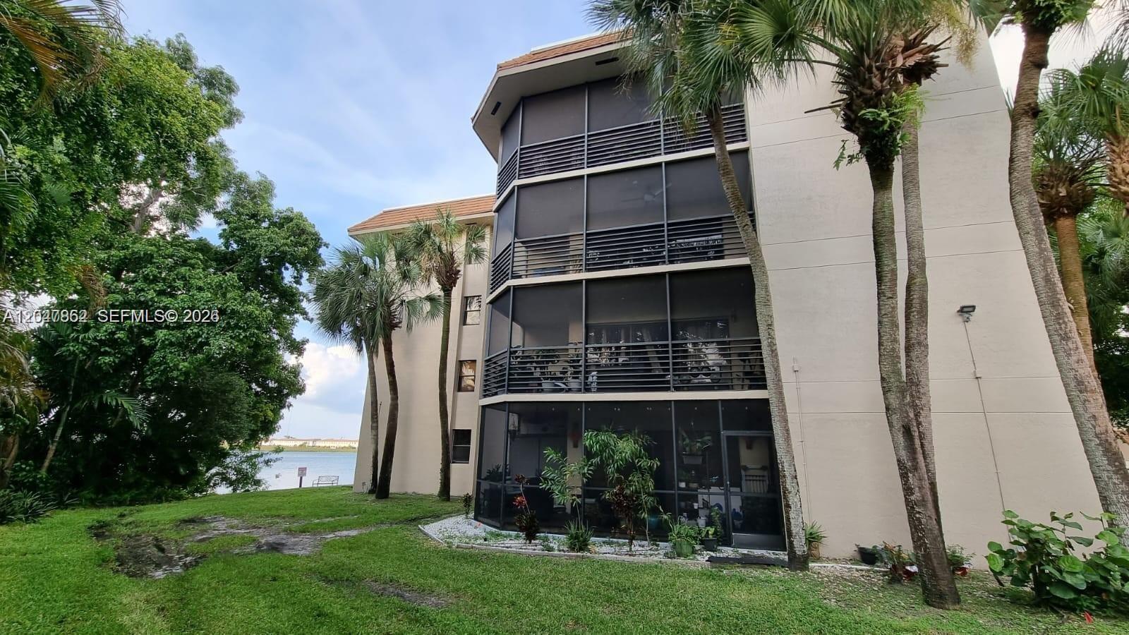 A multi-story apartment building with screened-in balconies overlooks a grassy lawn and a lake — 461 Ives Dairy Rd # 2, Miami FL 33179, MIAMI, FL