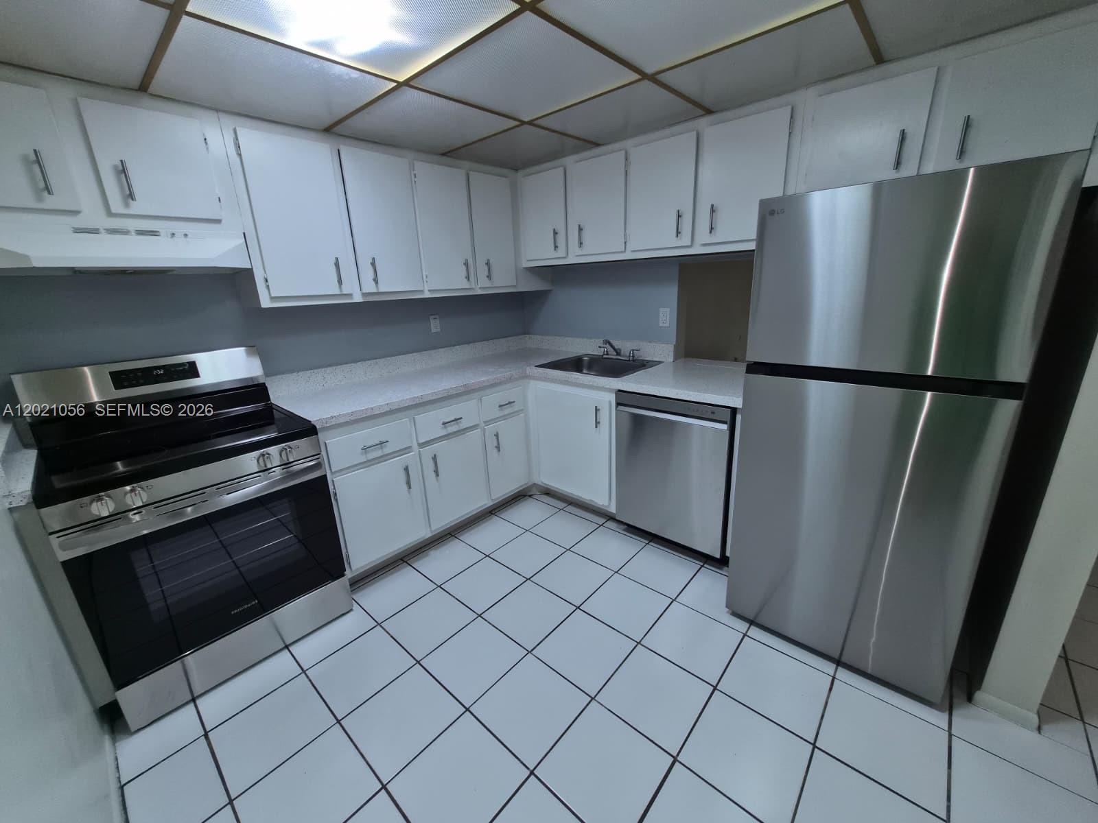 A kitchen featuring white cabinets, stainless steel appliances, light countertops, and white tiled flooring — 7830 Camino Real # 110, Miami FL 33143, MIAMI, FL