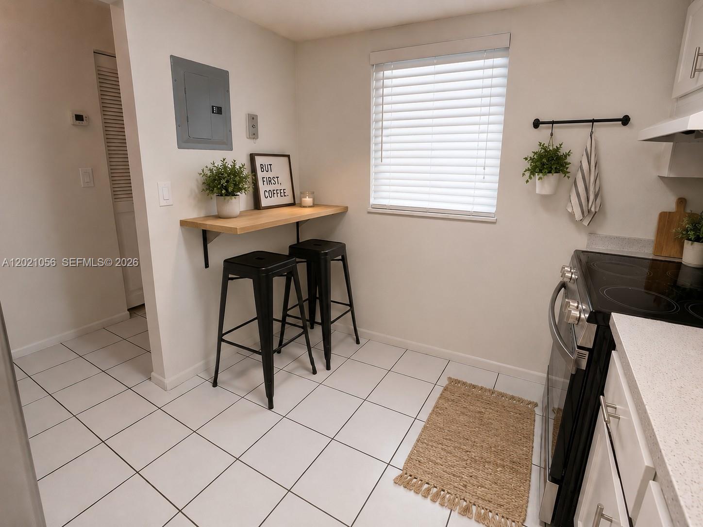 A kitchen features a wall-mounted breakfast bar with two black stools and white tile flooring — 7830 Camino Real # 110, Miami FL 33143, MIAMI, FL