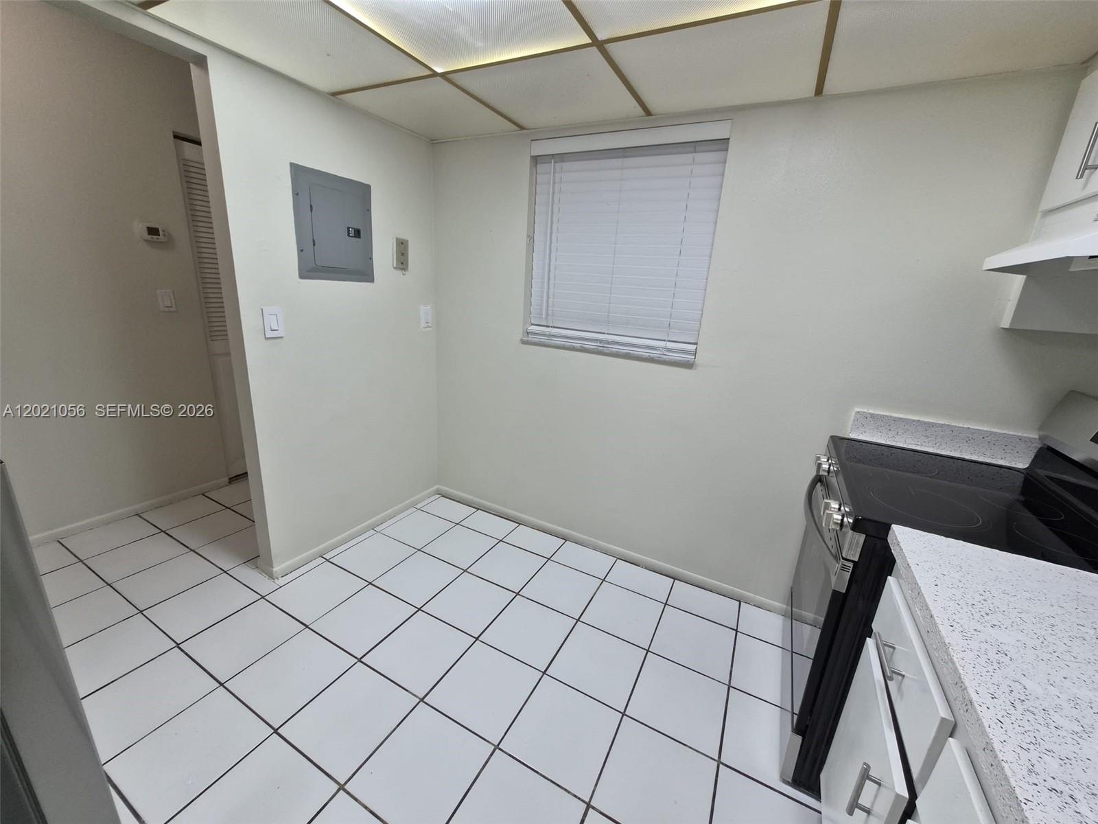 A kitchen features white tiled floors, a window with blinds, and a black electric stove — 7830 Camino Real # 110, Miami FL 33143, MIAMI, FL
