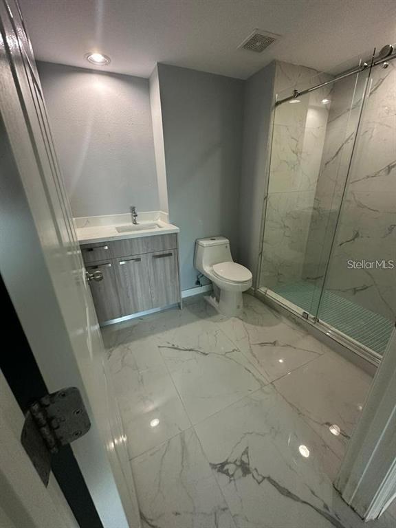 A modern bathroom features a wood-finish vanity, a white toilet, and a glass-enclosed marble shower — 322 E CENTRAL BOULEVARD UNIT 905, ORLANDO, FL