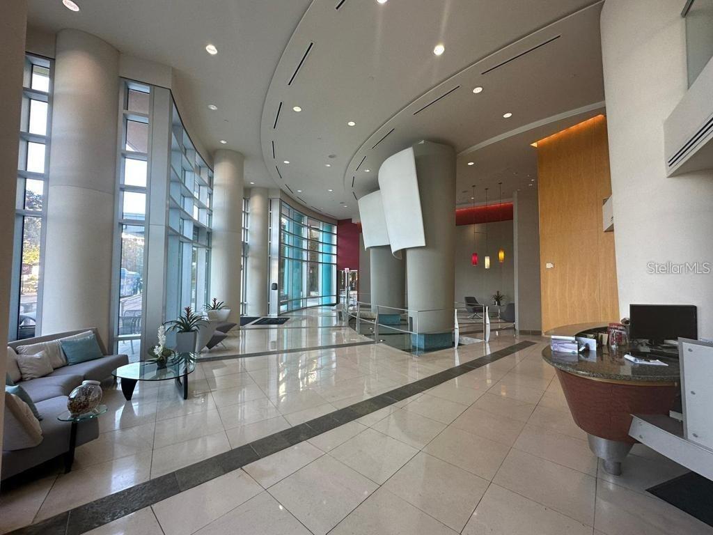 A modern building lobby features a reception desk, seating area, floor-to-ceiling windows, and tile flooring — 322 E CENTRAL BOULEVARD UNIT 905, ORLANDO, FL