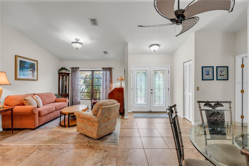 A living room with tile floors, an orange sofa, and a glass-paned double entry door — 19217 ABHENRY CIRCLE, PORT CHARLOTTE, FL