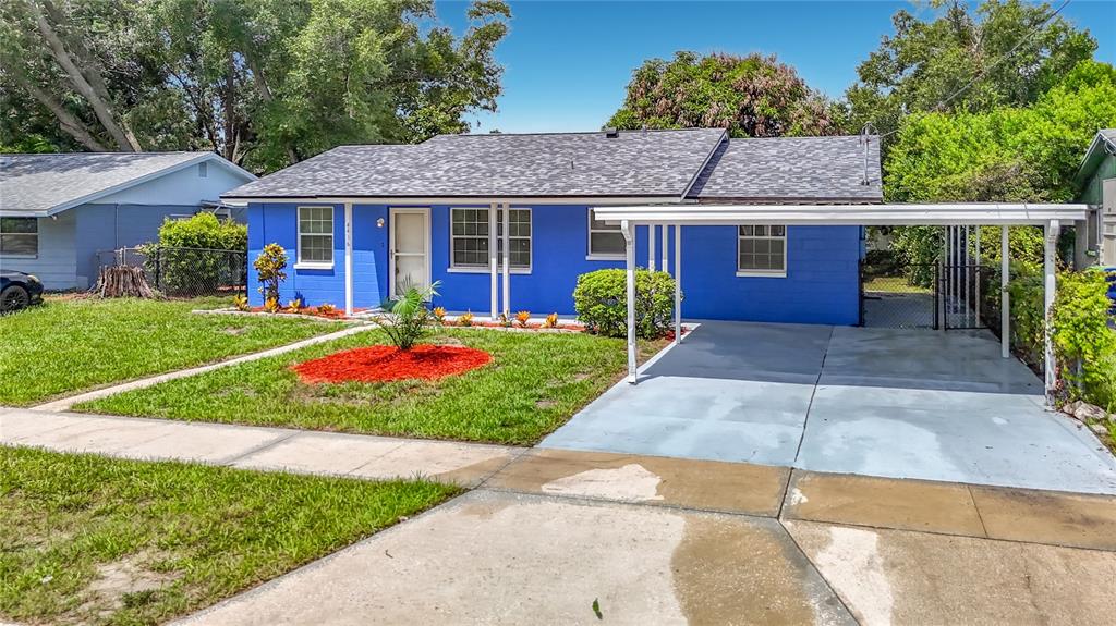 A bright blue single-story house with a gray roof and an attached white metal carport — 4416 N JOHN BELL JR DRIVE, TAMPA, FL