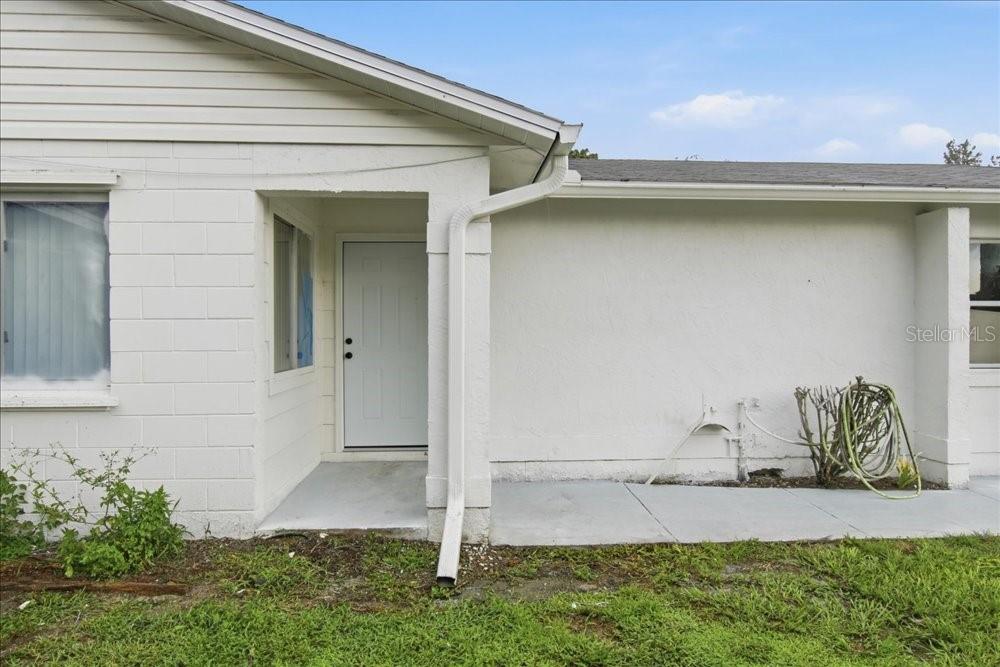 A white exterior wall features a recessed entryway with a door and a concrete walkway — 8612 SPRING CONE COURT, ORLANDO, FL