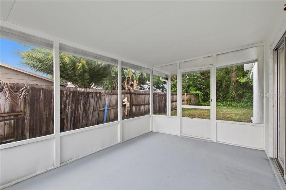 A screened-in porch with a gray concrete floor, white framing, and a wooden fence outside — 8612 SPRING CONE COURT, ORLANDO, FL