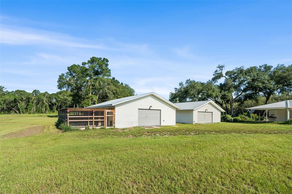 A detached garage with an attached outdoor kennel sits in a large, grassy field — 12450 NW 85TH AVENUE, CHIEFLAND, FL